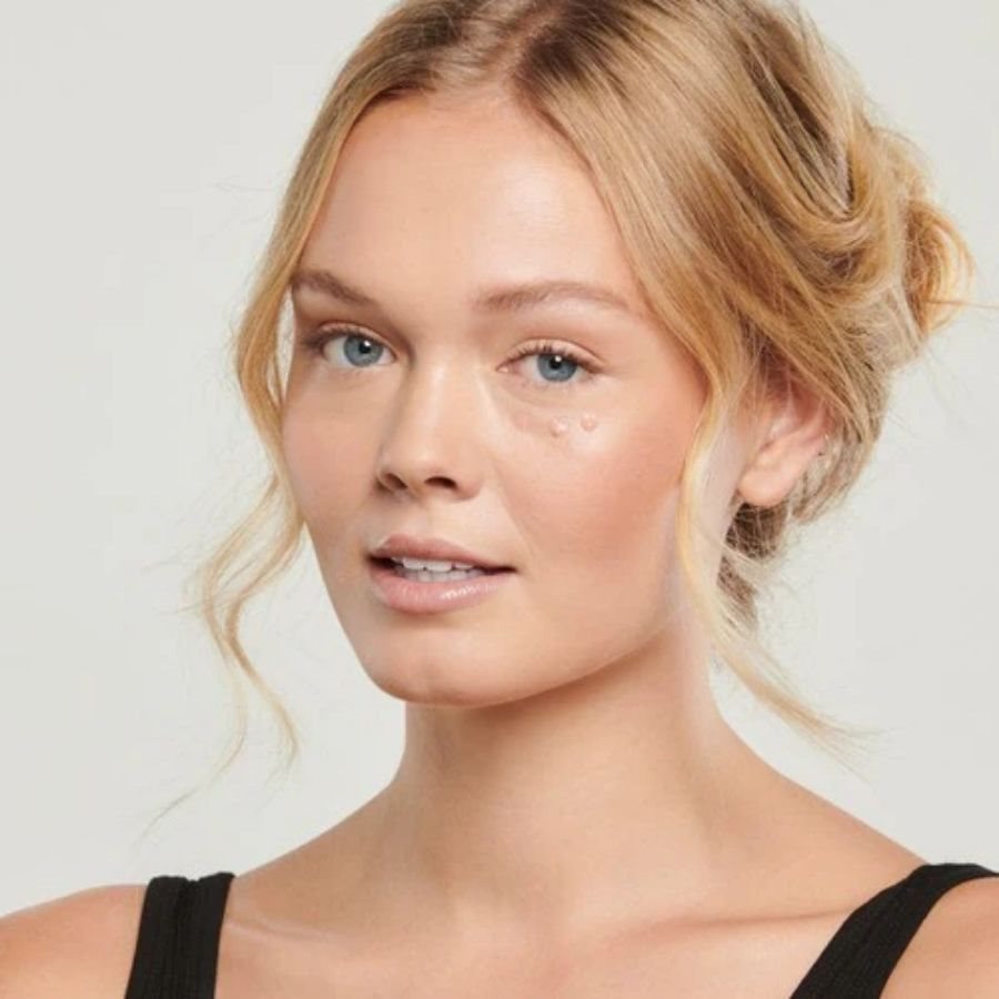 Woman with blonde hair styled in an updo against a plain background with Total Eye® 3-in-1 Renewal Care under left eye.