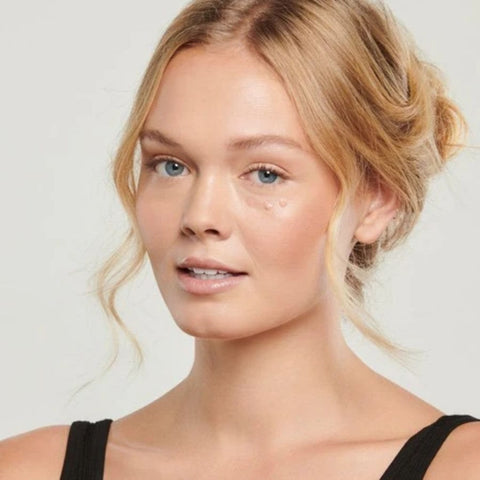 Woman with blonde hair styled in an updo against a plain background with Total Eye® 3-in-1 Renewal Care under left eye.