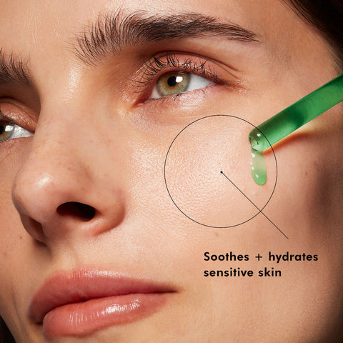 Close-up of a woman's face with a dropper applying green liquid to her skin, labeled 'Soothes + hydrates sensitive skin'.