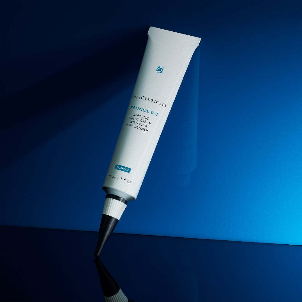 A squeeze tube of SkinCeuticals Retinol 0.3 Night Cream, shown diagonally against a dark blue background with a reflective surface below.